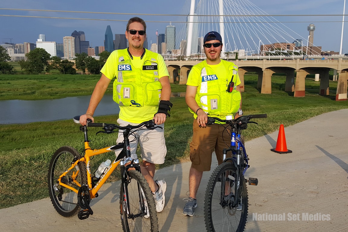 Two NSM EMS paramedics on bicycles with the Dallas skyline behind them