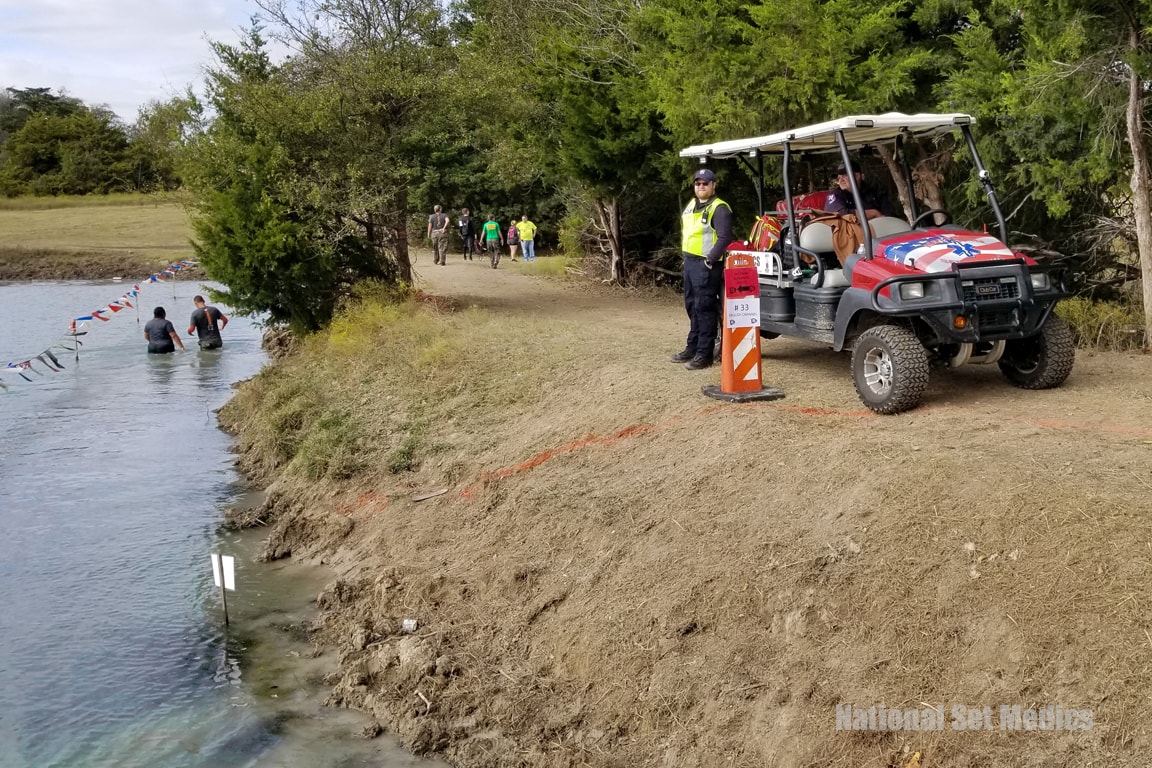 NSM medic standing by a waterway obstacle course with a golf cart